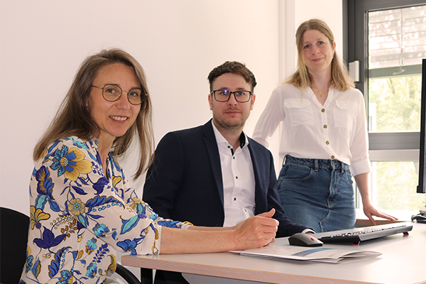 3 Personen sitzen am Tisch.